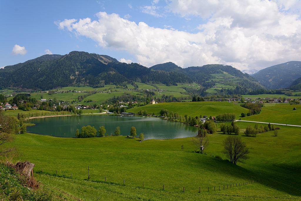 Natural lake with mountains in the background, green surroundings.